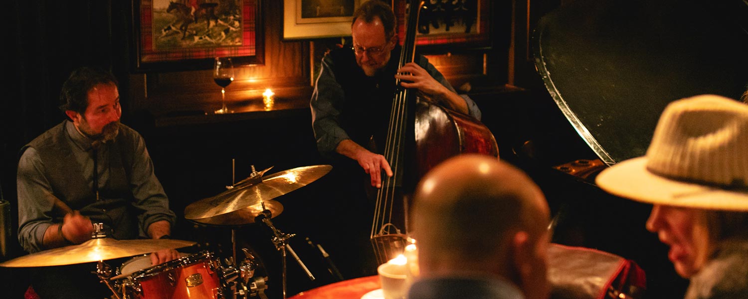 Two jazz musicians play in a lounge while patrons look on from a nearby table.