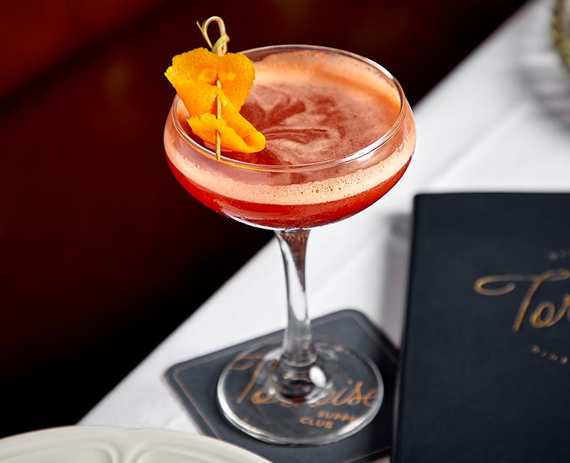 A cocktail with an orange garnish sits on a table